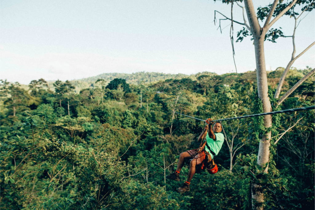 man hanging on wire above forest