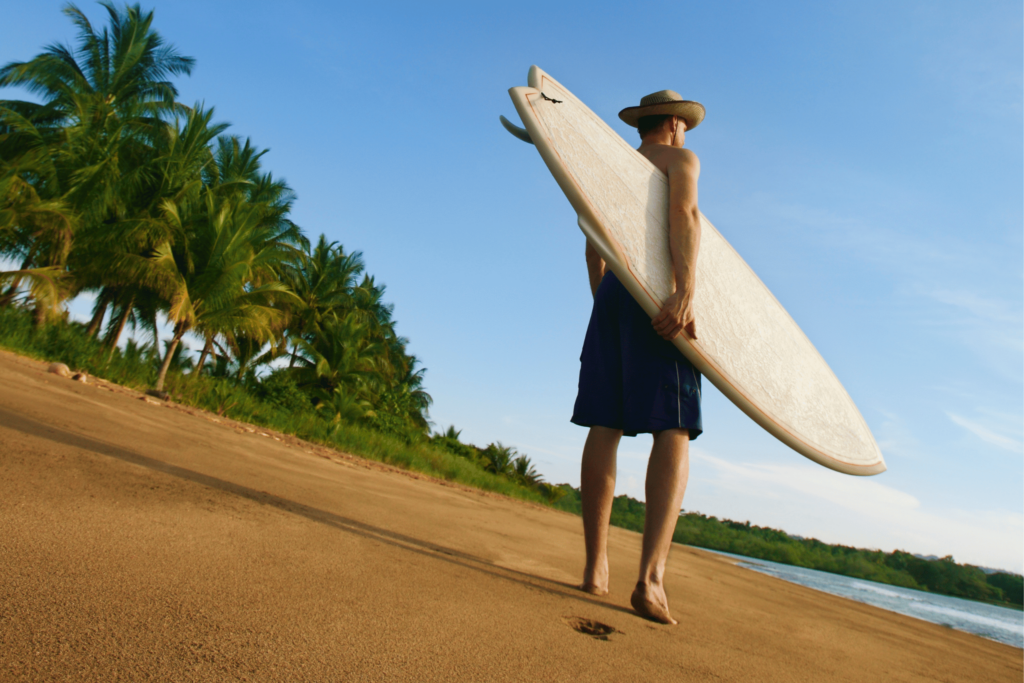 man walking on beach with surfboard
